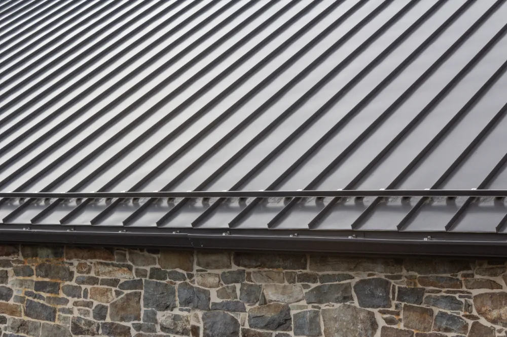 Dark gray standing seam metal roof on a Maine home with stone siding and durable weather-resistant panels.