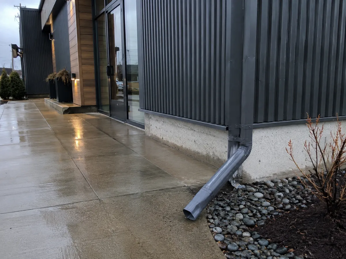 Downspout routed cleanly away from a commercial entry walkway, dry pavement