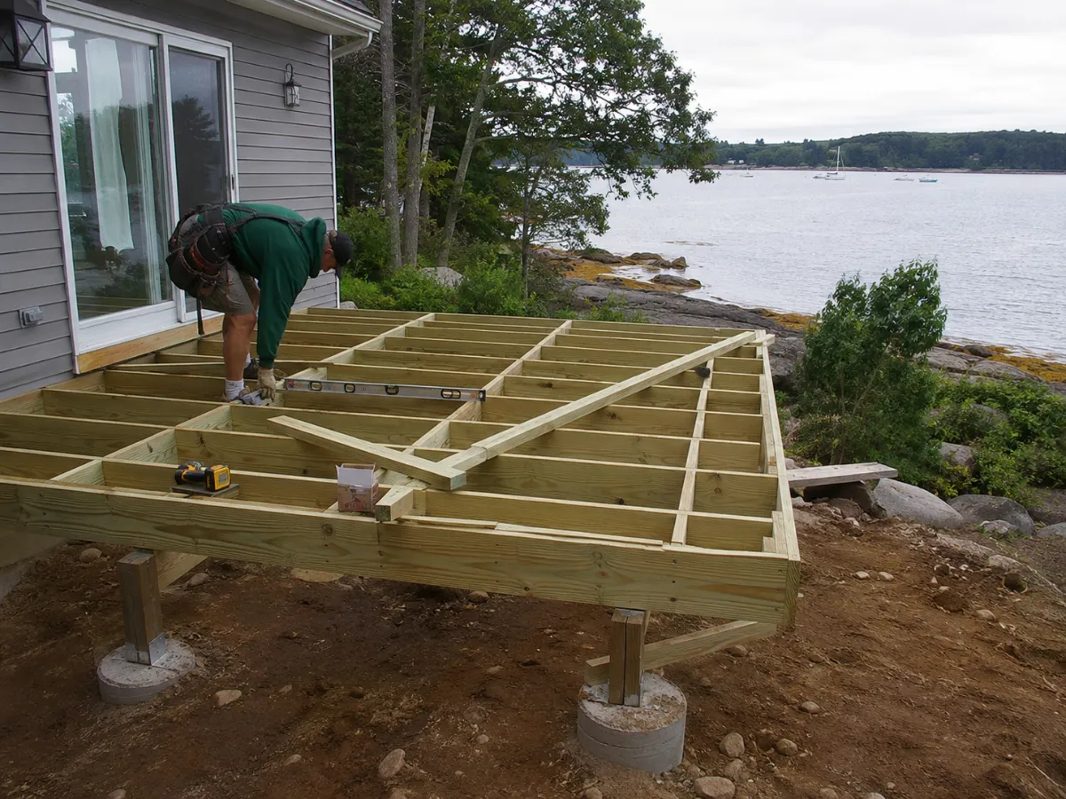 Builder framing a deck, pressure-treated structure and footings visible, honest construction