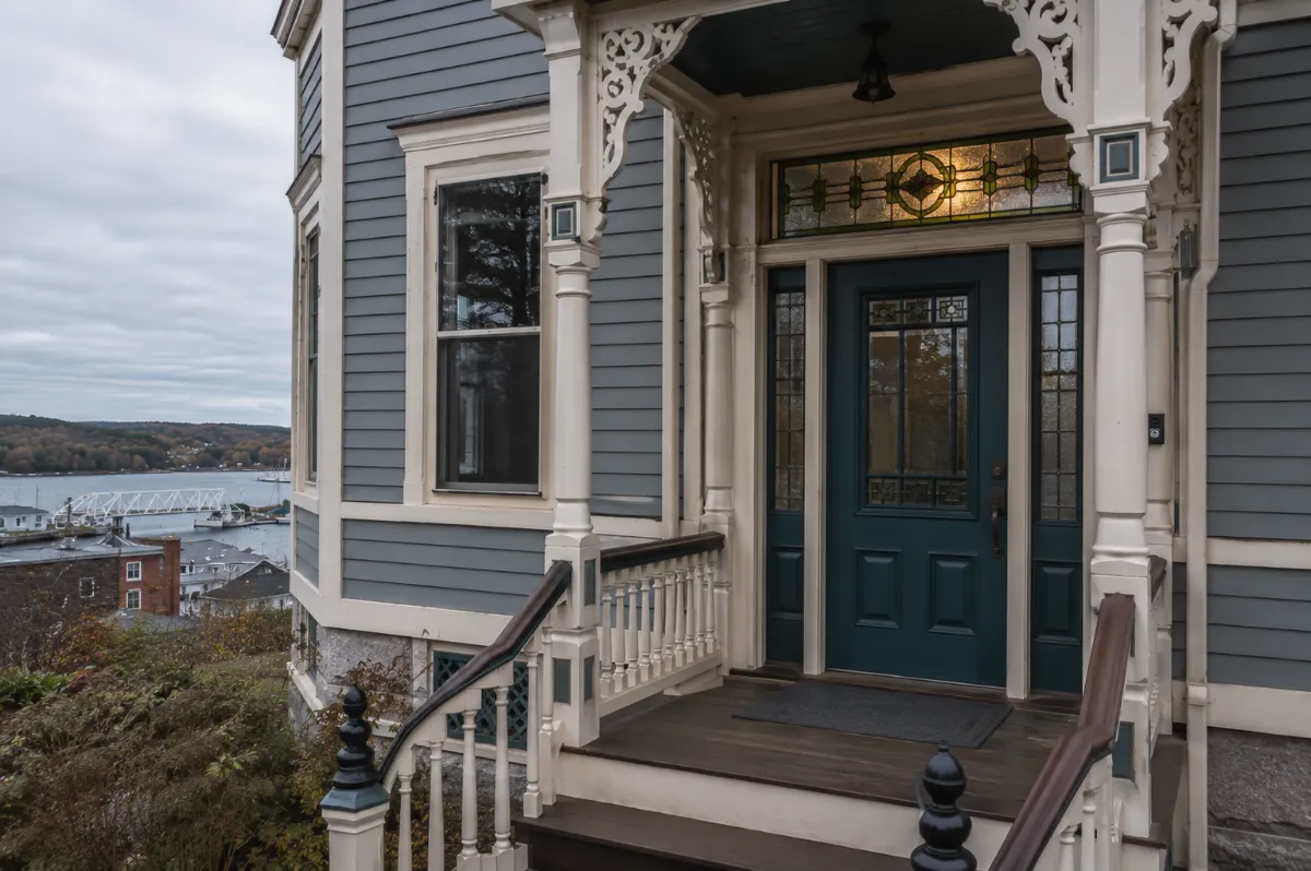 Deep teal Victorian entry door with a stained-glass transom on a Belfast home, ornate porch millwork freshly painted