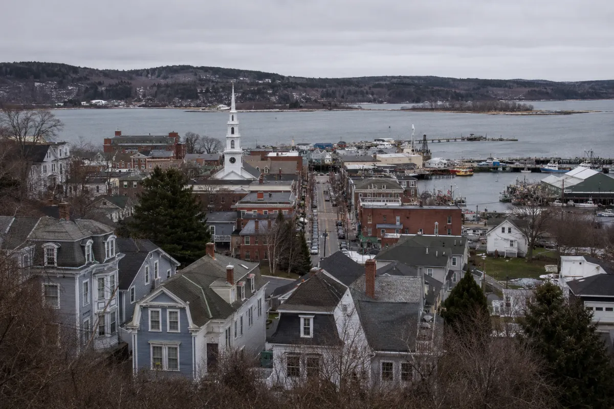 Hillside of Victorian and Greek Revival homes stepping down to Belfast Maine's working harbor on Penobscot Bay, brick Main Street and a church steeple in view