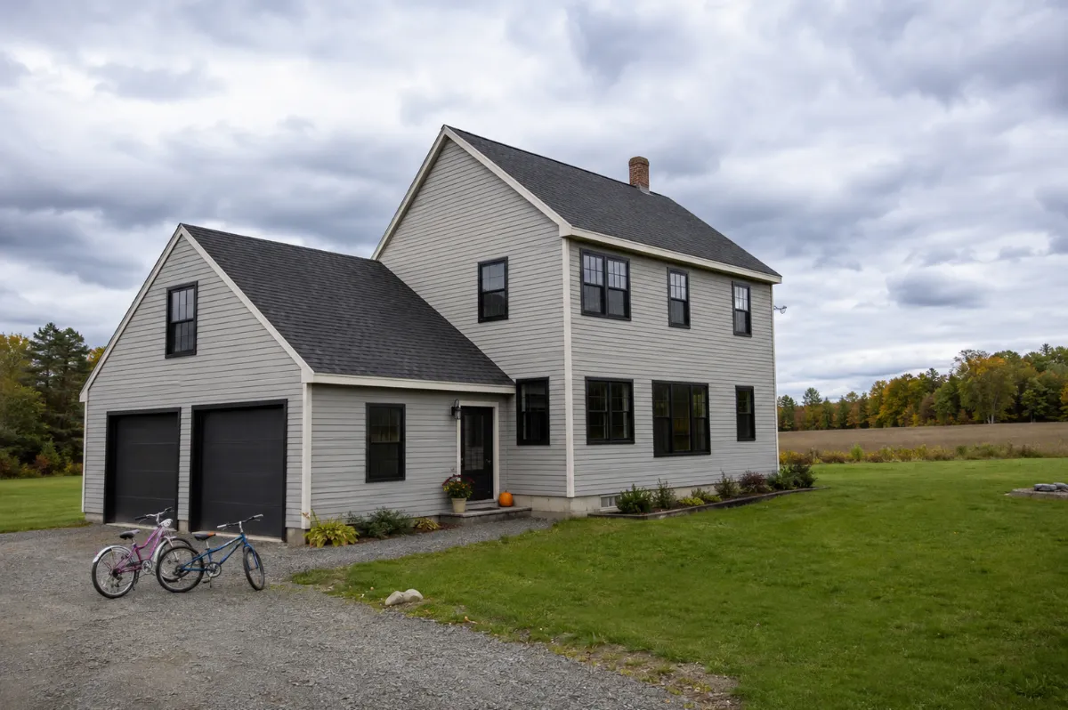 New black-frame windows on a Hermon family home, kids' bikes in the driveway, wide open sky behind