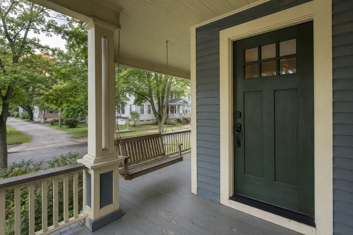 Sturdy craftsman entry door on an Orono front porch with a porch swing, leafy campus-town street beyond